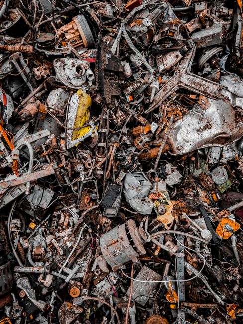 An outdoor scene showing litter scattered across a patch of grass and dirt near a concrete wall. The debris includes crushed, torn, and discarded cardboard boxes, some of which display green and white